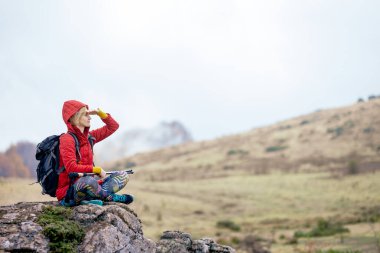 Yürüyüşçü kız dağlarda bir kayanın üzerinde dinleniyor. Manzaranın tadını çıkarıyorum. Gezi ve sağlıklı yaşam tarzı sonbahar mevsiminde açık havada