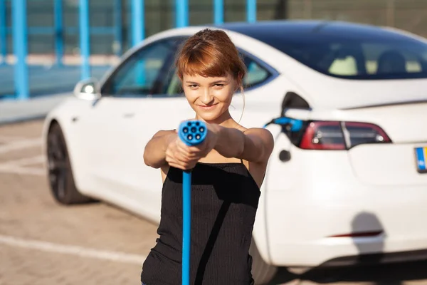 Gyönyörű Fiatal Lány Egy Elektromos Autó Mellett Töltőkábel Elhelyezése Tartása — Stock Fotó