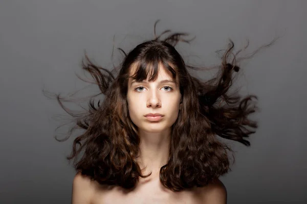 灰色の背景に美しい若い女の子のスタジオの肖像画 カメラを見て 風の強い髪 — ストック写真