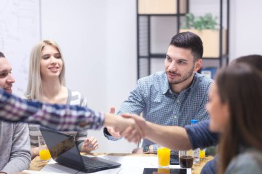 Modern işyerindeki bir grup genç, yaratıcı bir toplantı yapıyorlar, el sıkışıyorlar.