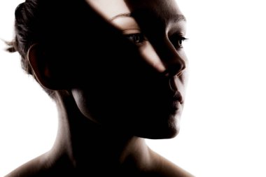 Şirin bir kızın moda stüdyo portresi. Yüzünde sert gölgeler olan güzel bir kadının silueti beyaz arka planda..