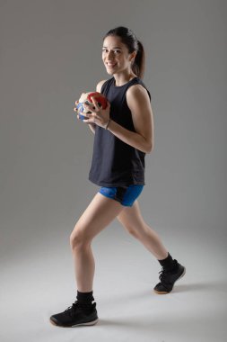 Hentbolcu açık gri arka planda poz veriyor. Topla poz veren kız.