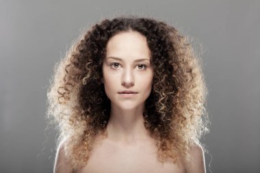 Uzun kıvırcık saçlı güzel esmer kız. Gri arkaplanda stüdyo resmi
