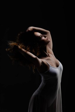 Kıvırcık saçlı kız bale pozu veriyor. Siyah arka planda beyaz elbiseli balerin silueti..