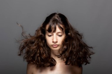 Gri arka planda güzel bir genç kız stüdyo resmi. Kameraya bakıyorum. Rüzgarlı saçlar.