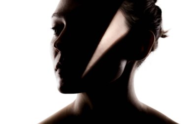 Şirin bir kızın moda stüdyo portresi. Yüzünde sert gölgeler olan güzel bir kadının silueti beyaz arka planda..