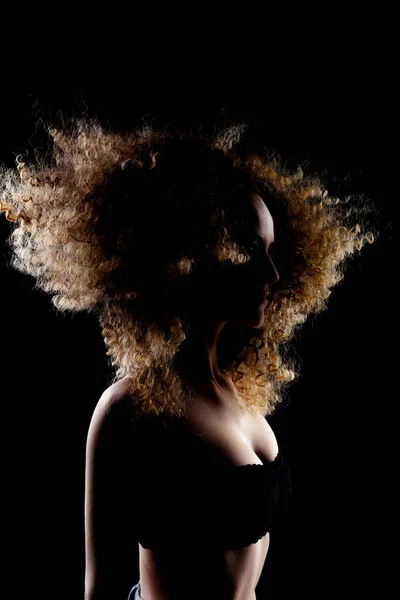 侧面点亮的黑发女孩 长长的卷发飘扬在空中 黑暗背景的轮廓工作室肖像 — 图库照片