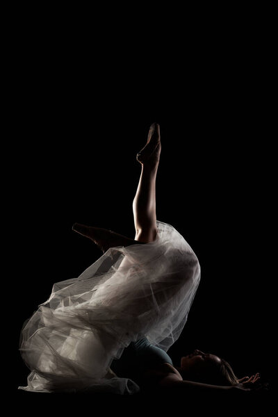 Ballerina with a white dress and black top posing on black background. side lit silhouette