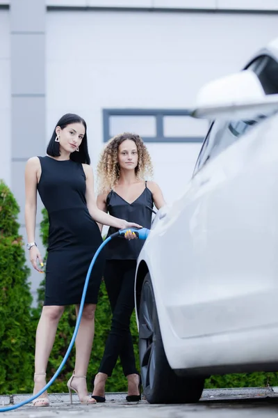 Dwie Piękne Bizneswoman Czarnym Outfut Pozowanie Obok Elektrycznego Samochodu Dziewczyny — Zdjęcie stockowe