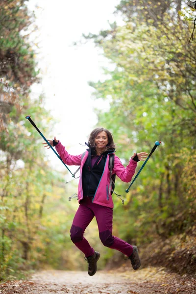 远足的女孩在山上的小径上跳着 背包客 带着远足杆和粉色夹克在森林里 户外运动快乐 — 图库照片
