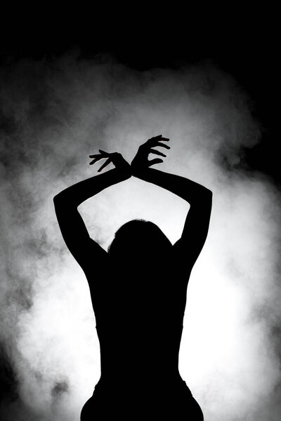 Silhouette modern ballet dancer posing on dark background with smoke