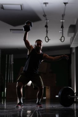 Çok ağır ağırlık kaldıran kaslı bir atletin silüeti. Adam içeride çalışıyor.