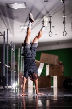 Ayakta duran ve baş aşağı yürüyen kaslı bir sporcu.