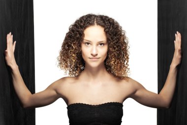 Uzun kıvırcık saçlı güzel esmer kız ayakta duruyor. Siyah çizgili stüdyo portresi.