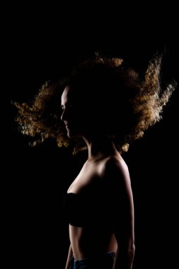 Havada uzun kıvırcık saçlı esmer kız. Karanlık arka planda siluet stüdyo portresi.