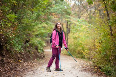 Dağlarda geniş bir patikada duran yürüyüşçü kız. Ormanda pembe ceketli bir sırt çantalı. Açık havada sağlıklı bir yaşam tarzı..