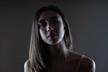 Güzel esmer kız stüdyo resmi. Koyu arkaplanda yarım siluet var. Ciddi yüz ifadesi.