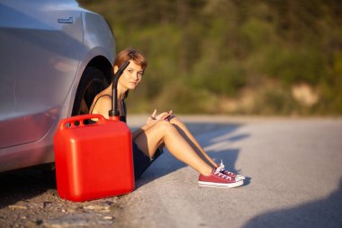 Üzgün kız yerde, kırmızı gaz tüplü elektrikli arabanın yanında oturuyor. Telefon bekletiliyor. 