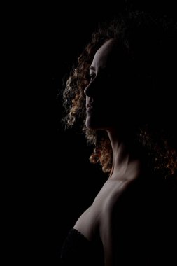 Uzun kıvırcık saçlı esmer kız, koyu arkaplanda siluet stüdyo resmi..