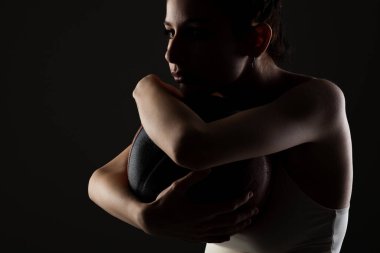 Basketbol oynayan genç bir kız. Stüdyonun karanlık arka planında yan ışıklandırılmış portresi.