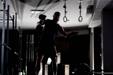 Çok ağır ağırlık kaldıran kaslı bir atletin silüeti. Adam içeride çalışıyor..