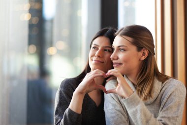 Bir kafede sarılıp pencereden dışarı bakan iki güzel kız. Elleriyle ocağı şekillendiriyorlar..