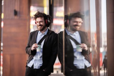 Sakar saçlı ve kulaklıklı bir adam pencerenin yanında yansımalı poz veriyor. Hipster tarzı iş adamı kahve molasında..