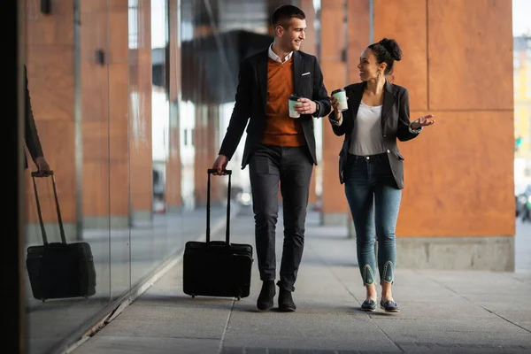 Business man and woman walking and drinking coffee. Businesspeople traveling together with luggage