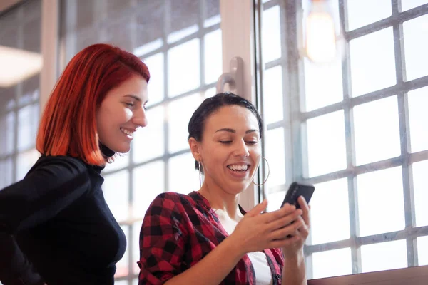 Két Lány Mosolyog Nézi Telefont Egy Ablak Mellett Egy Modern — Stock Fotó