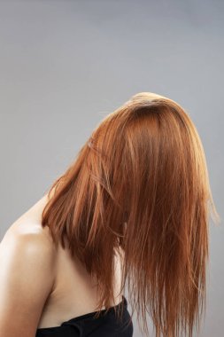 Koyu renkli, turuncu, rüzgarlı, gülümseyen güzel kız. Gri arkaplana karşı gülen yüz ifadesiyle stüdyo portresi.