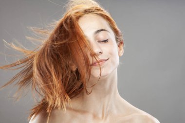 Koyu renkli, turuncu, rüzgarlı, gülümseyen güzel kız. Gri arkaplana karşı gülen yüz ifadesiyle stüdyo portresi.