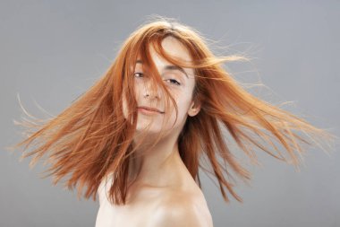 Koyu renkli, turuncu, rüzgarlı, gülümseyen güzel kız. Gri arkaplana karşı gülen yüz ifadesiyle stüdyo portresi.