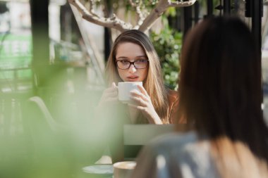 Bir kafede iki genç iş kadını teke tek görüşüyor. İşten sonra arkadaşlar dedikodu yapar ve güneşli bir günde cam kenarında kahve içerler..