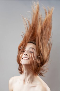 Koyu renkli, turuncu, rüzgarlı, gülümseyen güzel kız. Gri arkaplana karşı gülen yüz ifadesiyle stüdyo portresi.