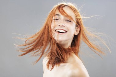 Koyu renkli, turuncu, rüzgarlı, gülümseyen güzel kız. Gri arkaplana karşı gülen yüz ifadesiyle stüdyo portresi.