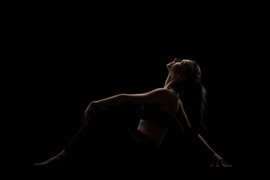Siyah arka planda yoga pozu veren beyaz bir kız. yan aydınlatma silueti.