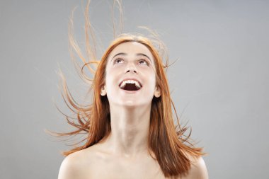 Koyu renkli, turuncu, rüzgarlı, gülümseyen güzel kız. Gri arkaplana karşı gülen yüz ifadesiyle stüdyo portresi.