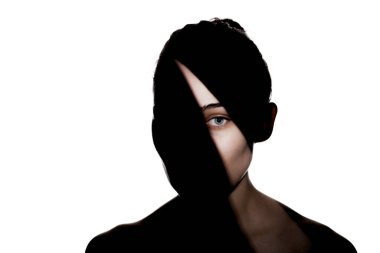 Şirin bir kızın moda stüdyo portresi. Yüzünde sert gölgeler olan genç ve güzel bir kadının silueti. beyaz arka plana karşı.