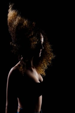 Havada uzun kıvırcık saçlı esmer kız. Karanlık arka planda siluet stüdyo portresi.