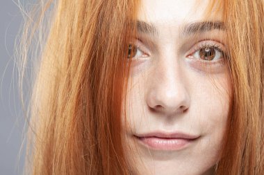 Güzel koyu turuncu saçlı kız kameraya bakıyor. Gri arkaplanda gülen yüz ifadesiyle stüdyo portresi.