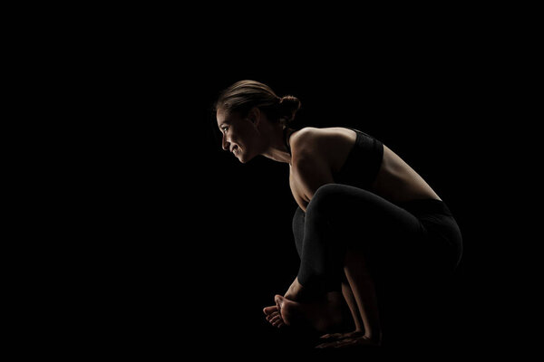 Cute caucasian girl exercising yoga poses against dark backgroung. side lit silhouette.