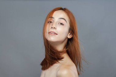 Koyu renkli, turuncu, rüzgarlı, gülümseyen güzel kız. Gri arkaplana karşı gülen yüz ifadesiyle stüdyo portresi.