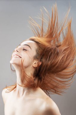 Koyu renkli, turuncu, rüzgarlı, gülümseyen güzel kız. Gri arkaplana karşı gülen yüz ifadesiyle stüdyo portresi.