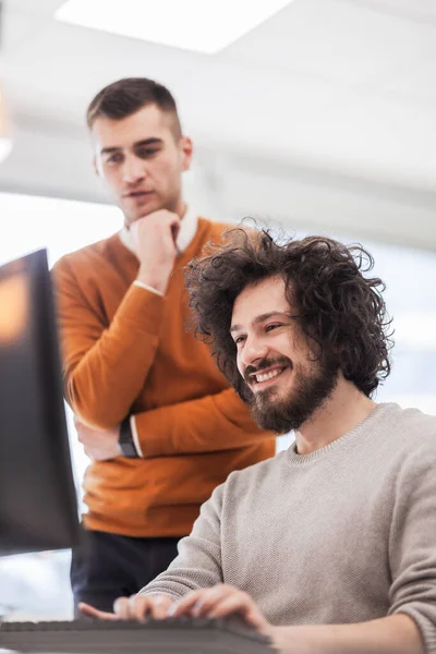 Business people having conversation in front of a computer in modern coworking office space.