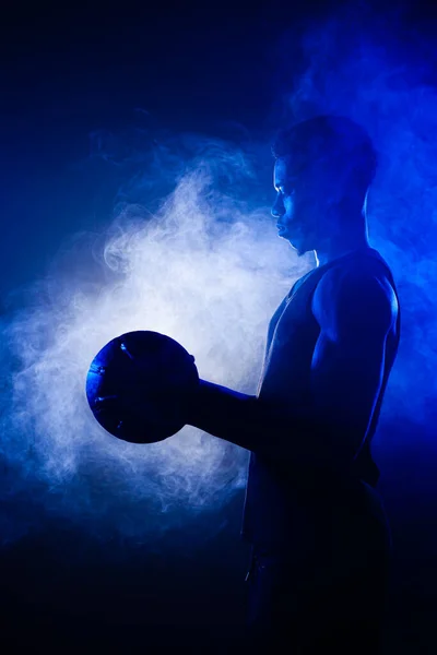 バスケットボール選手は青い霧を背景にボールを持っている アフリカ系アメリカ人のシルエット — ストック写真