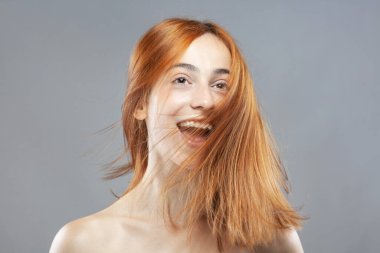 Koyu renkli, turuncu, rüzgarlı, gülümseyen güzel kız. Gri arkaplana karşı gülen yüz ifadesiyle stüdyo portresi.