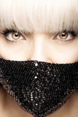 Sarışın, püsküllü, siyah, modaya uygun koruyucu yüz maskesi takan güzel esmer kız. Portreyi kapat. Gözler kameraya bakıyor.