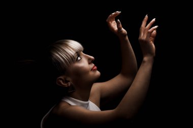 Sarı kaküllü güzel bir kız. Siyah arka planda beyaz, şık bir elbise giyiyor..