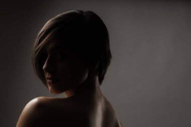 Güzel bir kızın karanlık, yarı gölgeli portresi. Gri arkaplanda kısa saç stili.