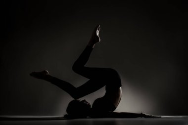 Fit balerin kız yalan söylüyor ve yoga pozları veriyor. Koyu arkaplana karşı yan aydınlatma silueti.